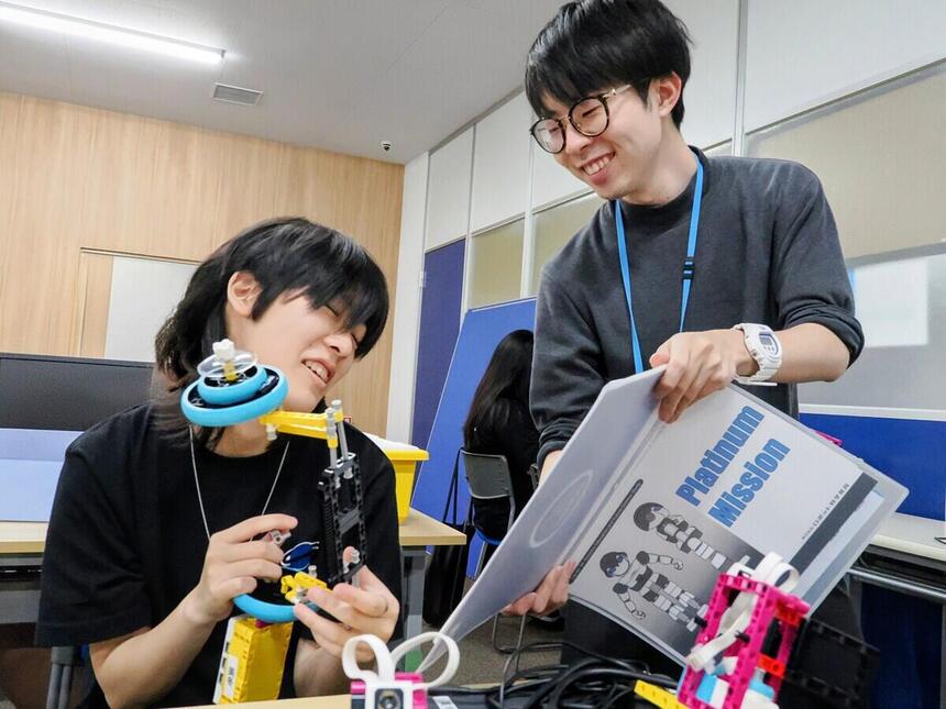 プログラミングコース時にテキストを見せる教師とそれを見る生徒