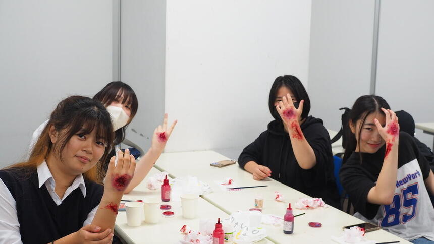 4人の女子生徒が腕に傷跡を模したメイクを施してポーズを決めている写真