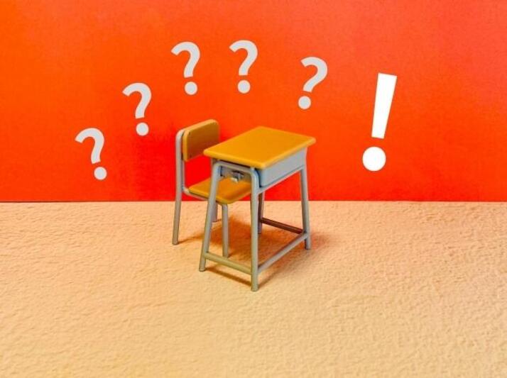 学校の机の周りにはてなマークとビックリマークが並んでいるイラスト