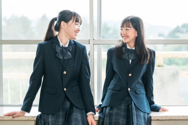 制服をきている女子生徒2人が、窓際で笑いながら話をしている