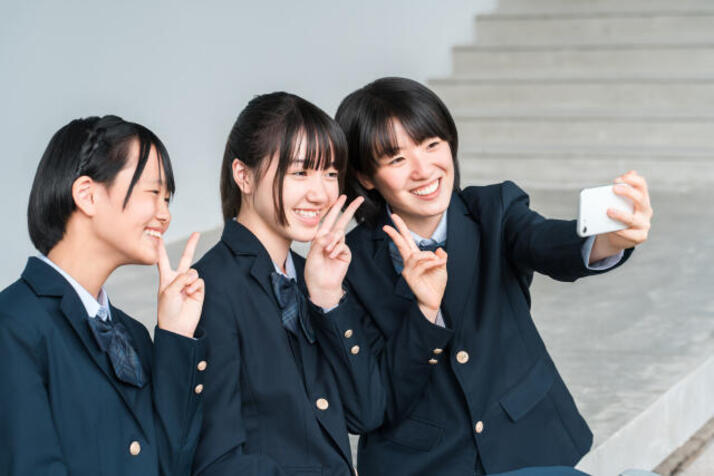 制服を着ている3人の女子生徒が階段の前で写真を撮っている様子