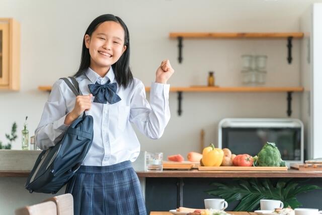 制服をした女子生徒がキッチンの前で笑顔でガッツポーズをしている