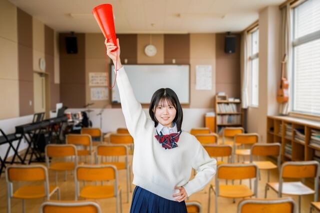 女子高校生がメガホンを持ち音楽室で腕を上げている姿