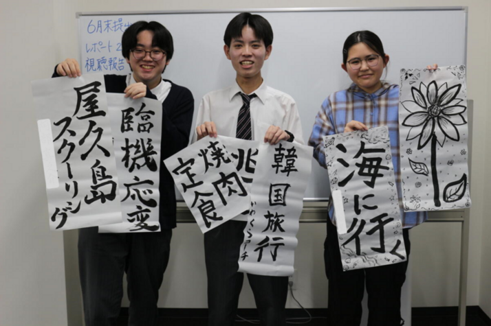 3人の生徒たちが自分で書いた習字を持って写真に写っている様子