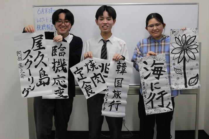 3人の生徒たちが自分で書いた習字を持って写真に写っている様子