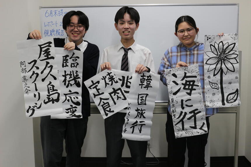 3人の生徒たちが自分で書いた習字を持って写真に写っている様子