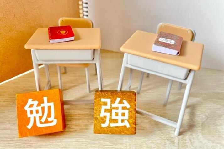 学校の教室の机が2つ並んでいる下に、「勉強」という漢字のパネルが並んでいて、学校での勉強を連想させる画像